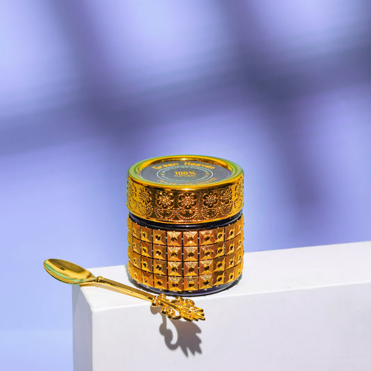 Decorative gold container with a matching spoon on a white platform against a purple gradient background